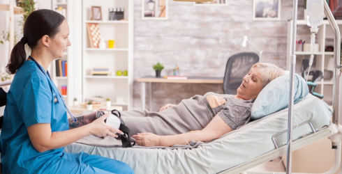 Post Operative Services. Nurse helping a patient who is lying in bed.