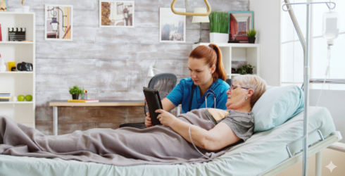 Female nurse helps patient lying in bed using digital tablet